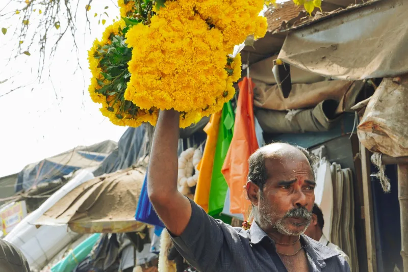 A vendor carrying marigold garlands through a market